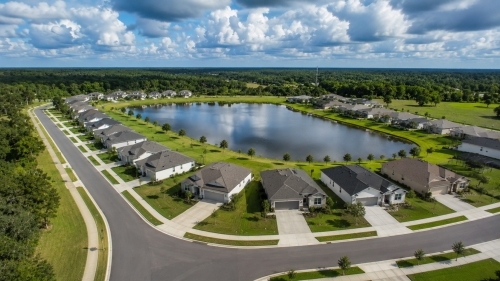 Aerial real estate drone view of a modern residential subdivision with clean street curves wrapping around a large community retention pond in Auburndale Florida.